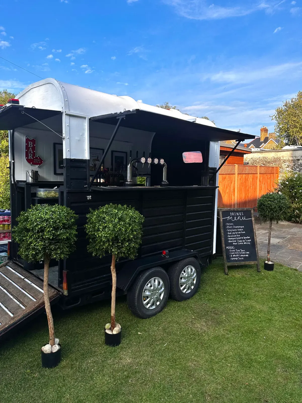 Little bars horsebox, chalkboard drinks menu and bay trees in the sunshine